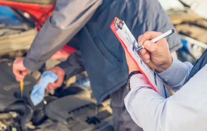 ADAS Services In Monticello AR At Strokers Diesel Performance & Repair. A person holds a clipboard and writes with a pen while another person checks under a car hood, suggesting a vehicle inspection or maintenance.
