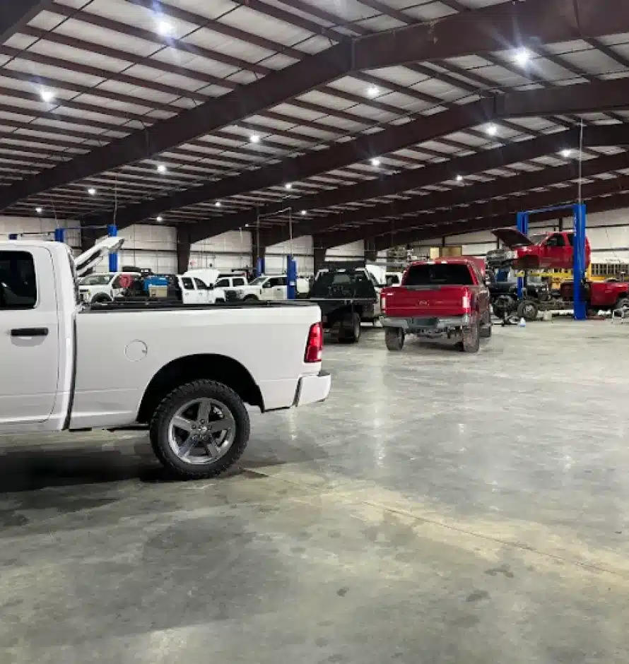 Auto Repair In Monticello AR At Strokers Diesel Performance & Repair. Large auto repair shop with high ceilings and overhead lights, several pickup trucks parked inside, some on lifts, and tools and equipment visible in the background.