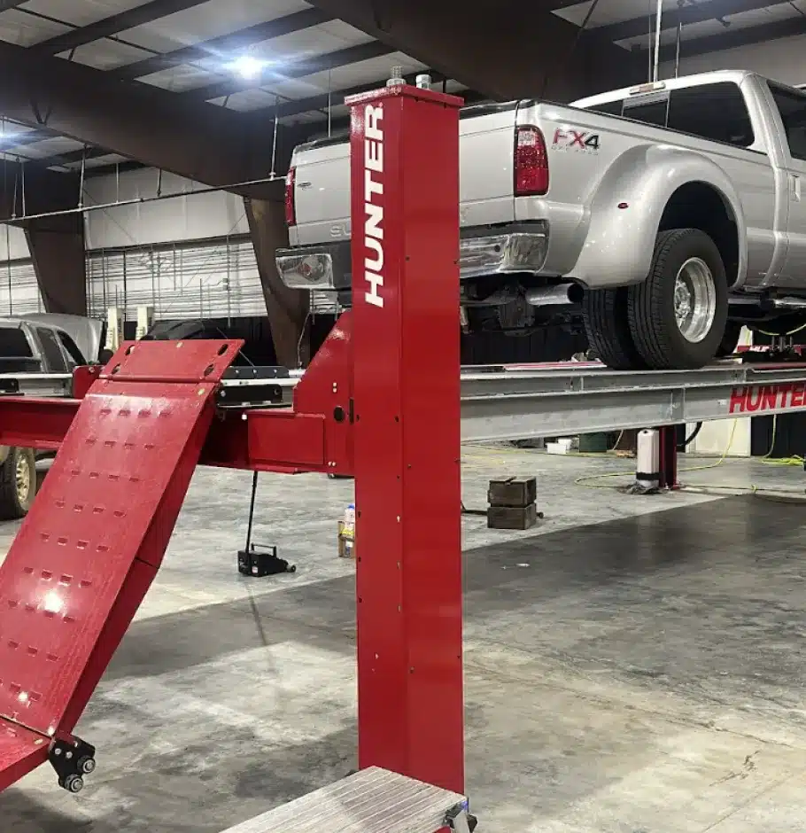 About Strokers Diesel Performance & Repair. A silver Ford Super Duty FX4 pickup truck is parked on a red Hunter vehicle lift inside a large, well-lit garage or workshop with a concrete floor.