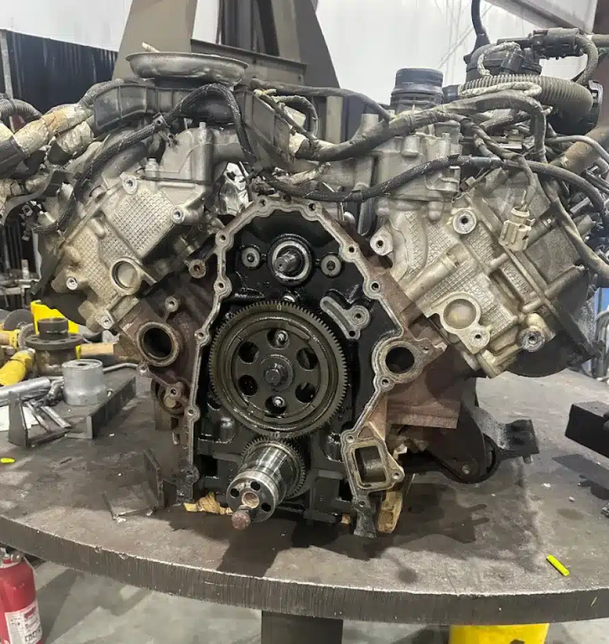 Engine Repair & Replacement In Monticello AR At Strokers Diesel Performance & Repair. A disassembled V-shaped engine sits on a workbench in a workshop, exposing its internal gears and components. Various tools and parts are scattered around the table.