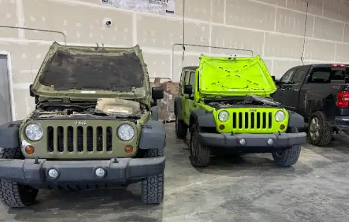 Vehicle Inspections In Monticello AR At Strokers Diesel Performance & Repair. Two green Jeep Wranglers with their hoods open are parked side by side inside a garage; a dark pickup truck is parked next to them on the right.