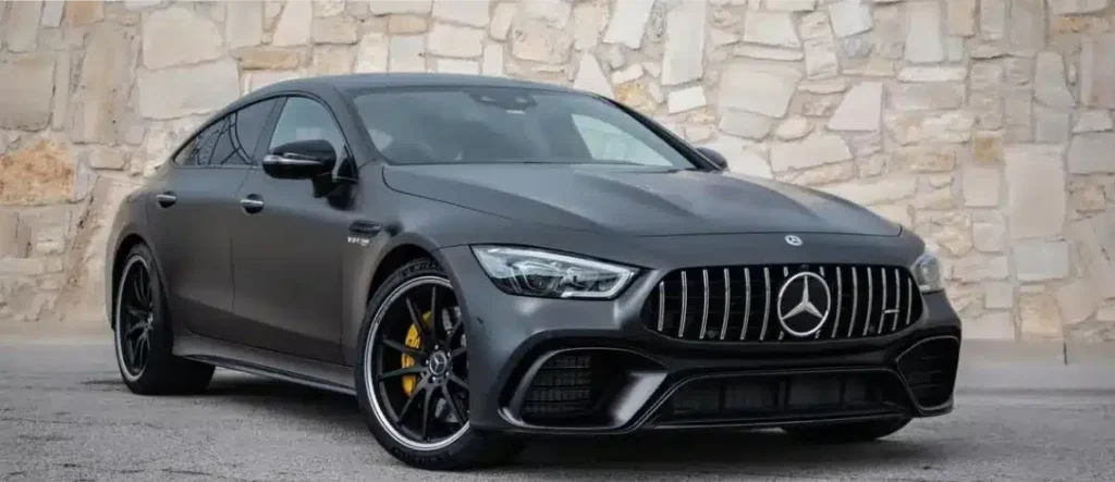European Vehicle repair In Monticello AR At Strokers Diesel Performance & Repair. A matte black Mercedes-Benz sports car with yellow brake calipers is parked on a concrete surface in front of a beige stone wall.