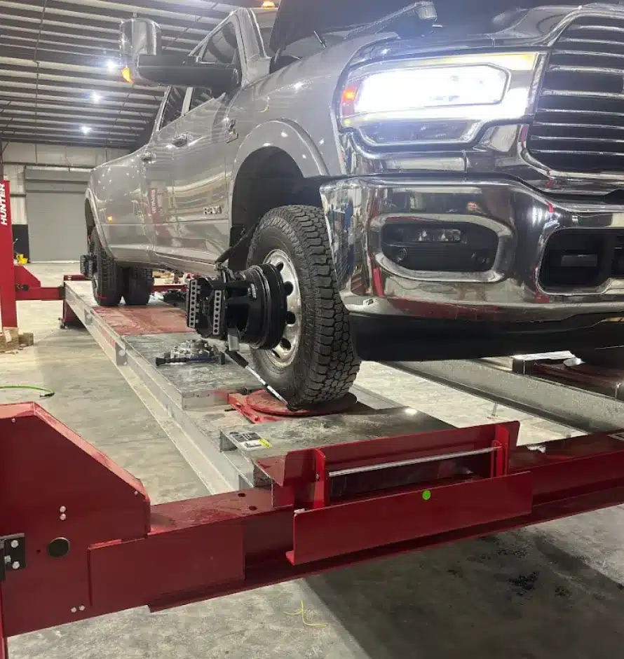 Wheel Alignment In Monticello AR At Strokers Diesel Performance & Repair. A gray pickup truck is elevated on a red alignment rack inside a garage, with its front wheels removed and alignment equipment attached to the hubs.