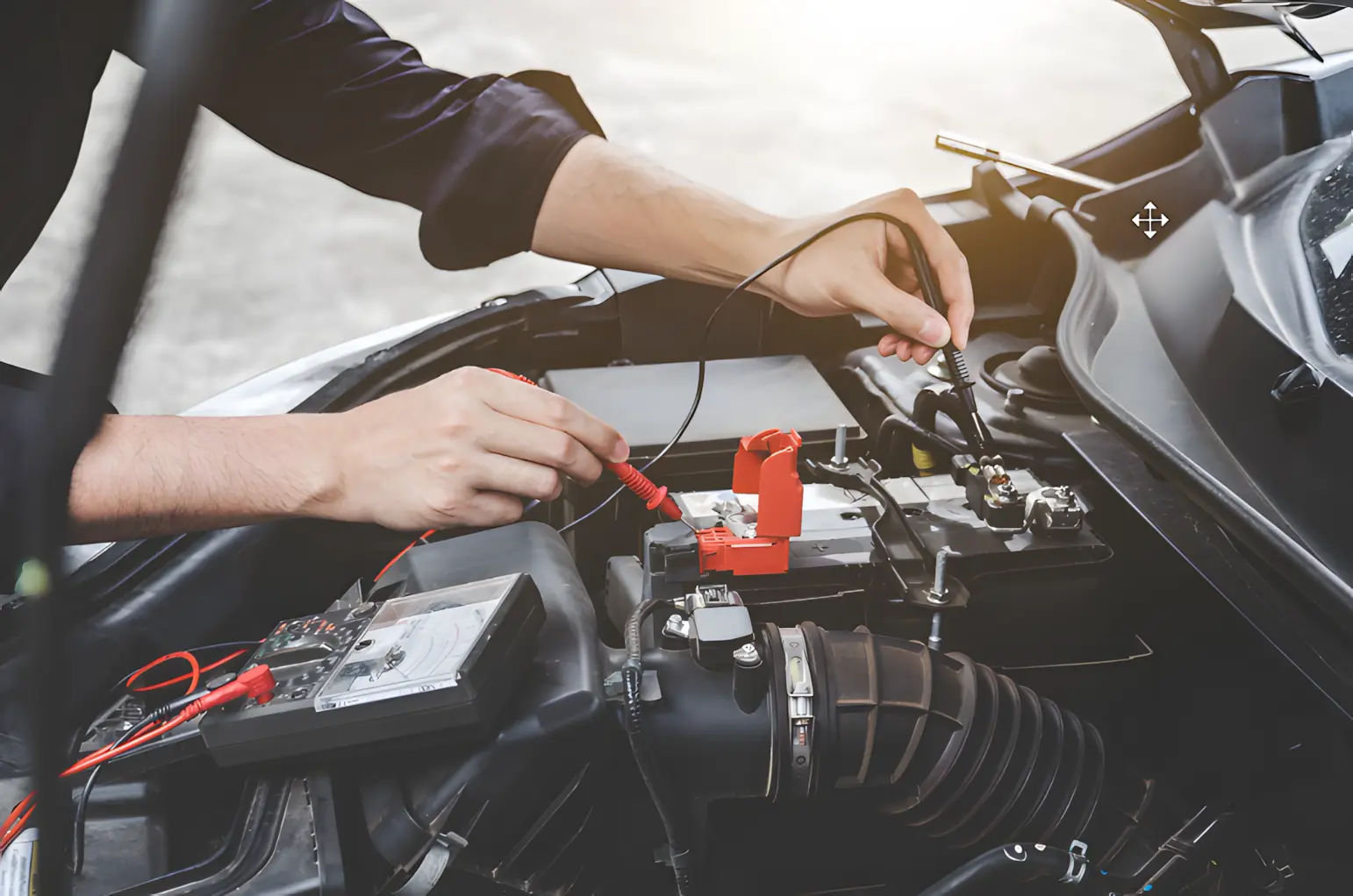 A person uses multimeter probes to check a car battery under the open hood of a vehicle. The scene focuses on their hands connecting the testing leads to the battery terminals and other engine components.