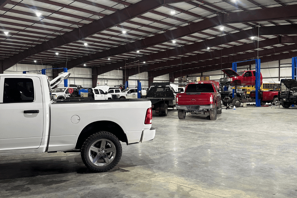 Vehicle inspection, diesel repair in Monticello, AR at Strokers Diesel Performance & Repair. Image of multiple pickup trucks inside a service facility, including one raised on a lift for maintenance.